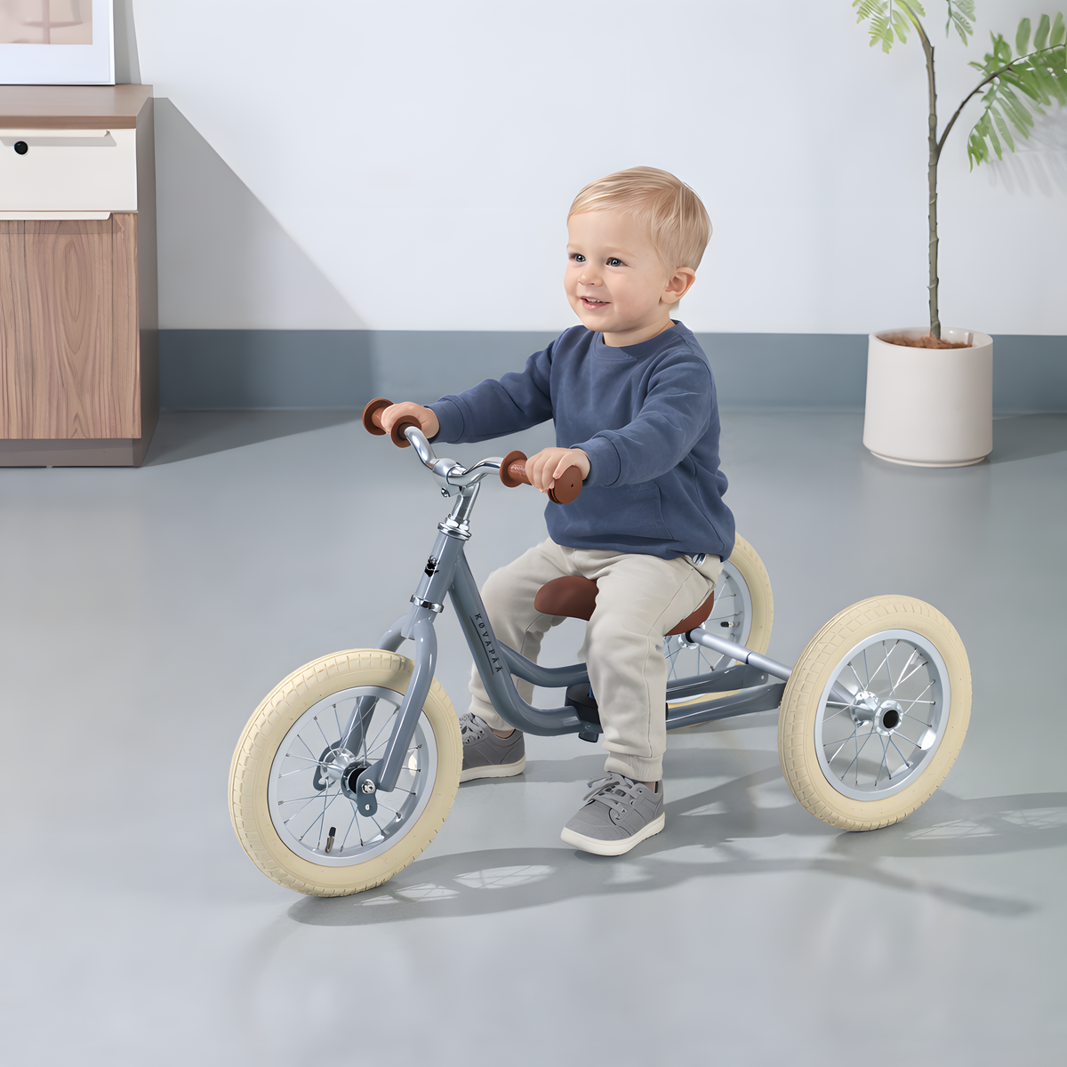 Kovapää 2 in 1 Loopfiets Grijs - Kind met een driewieler in een lichte ruimte, lachend en genietend.